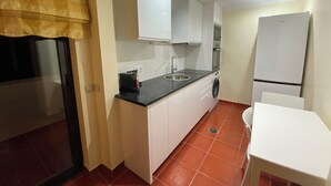 A compact kitchen with white cabinets, a black countertop, a sink, a washing machine, and a refrigerator.
