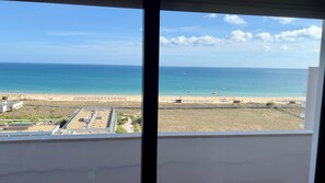 A view of a beach from a window overlooking a sandy area with a clear sky and calm sea.