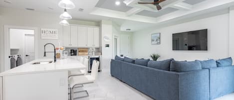 A modern kitchen with white cabinetry, a central island with bar stools, and a blue sofa in the living area.