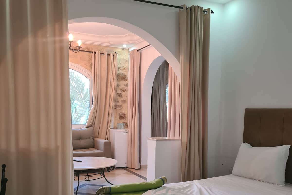 Una habitación de hotel con cama, sofá, una mesita y ventana con cortinas.