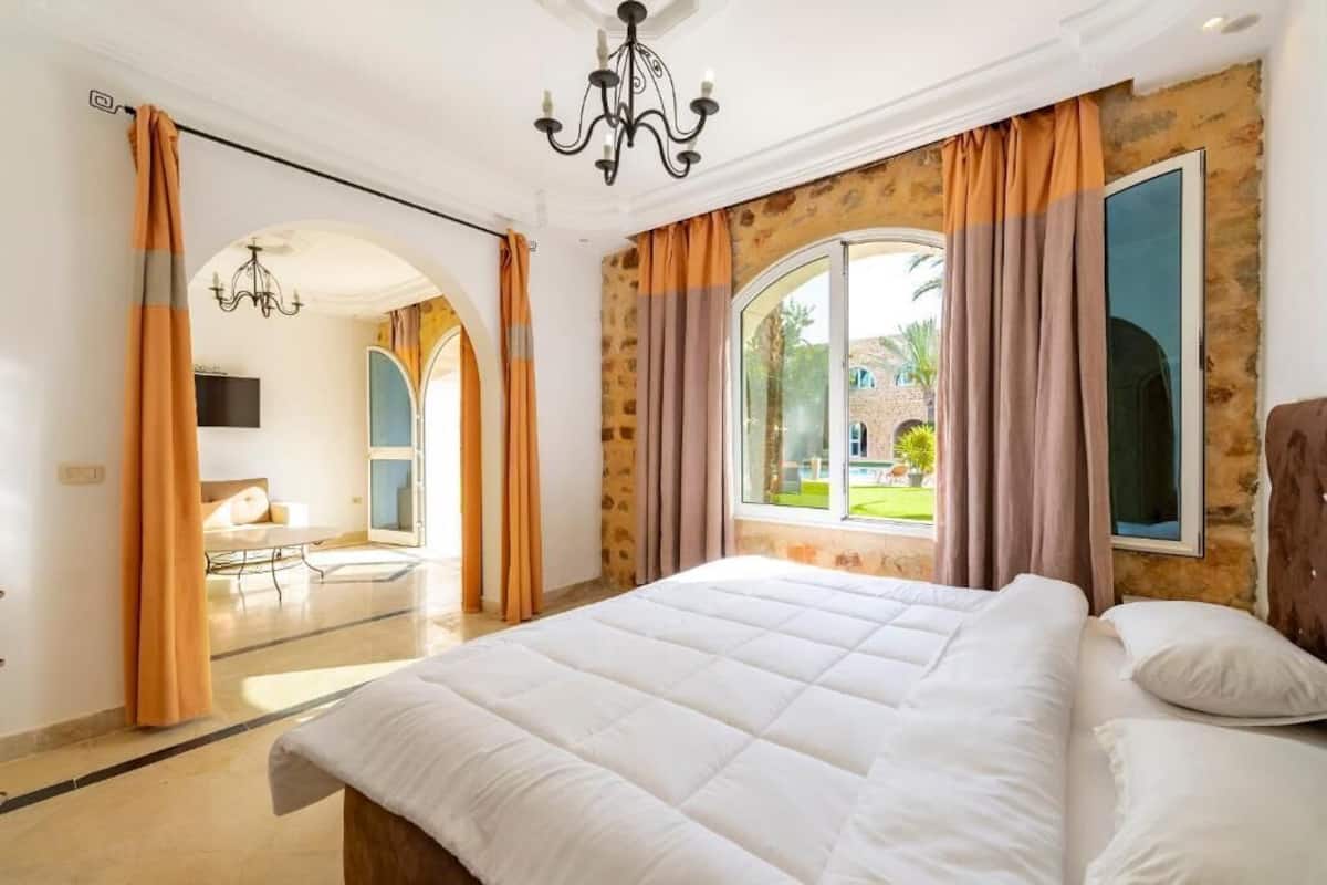 Un dormitorio con una cama grande, una araña y vistas a un jardín a través de una ventana.