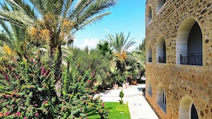 Un patio con palmeras, plantas con flores y un edificio de piedra con ventanas de arco.