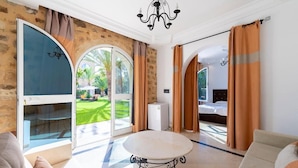 Una habitación amplia con un gran ventanal corredera que da a un jardín, una mesa redonda y una cama con cortinas.