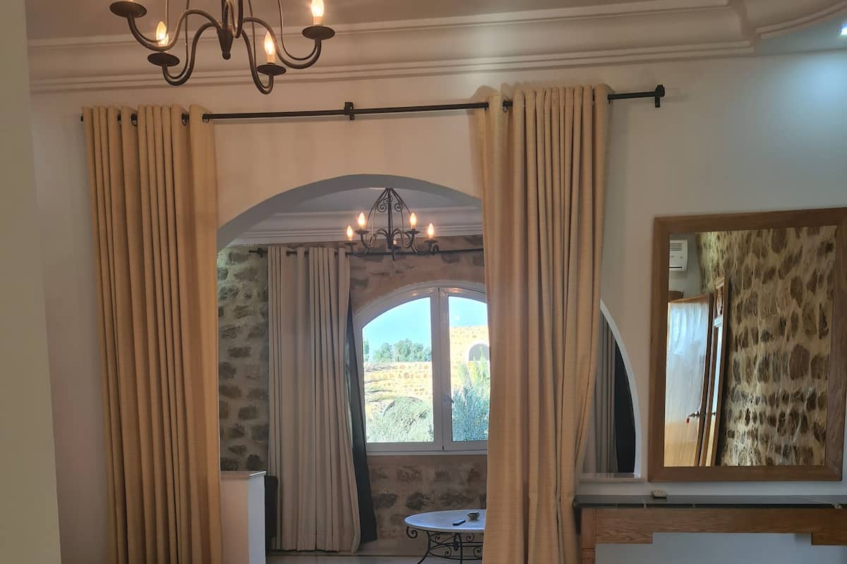 Un dormitorio con cama, una mesita, un espejo y vistas al exterior a través de una ventana.