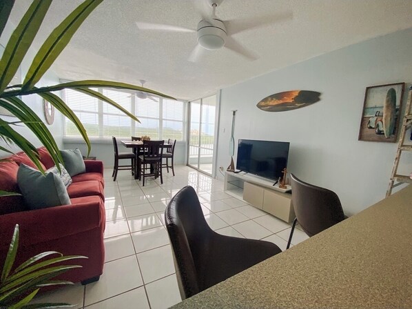 A spacious living room with a red sofa, a black chair, a dining table, and a TV.