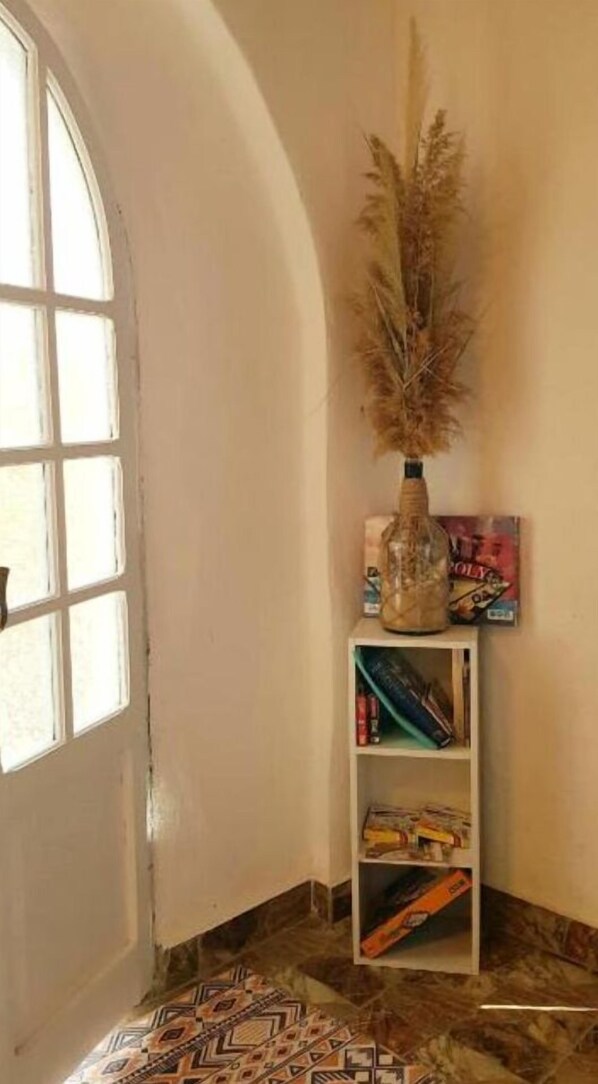 A corner room with a white door, a bookshelf with books and a decorative vase, and patterned floor tiles.