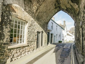 A narrow street with stone buildings, a visible window with a grid pattern, and a clear sky.