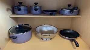 Keittiön hylly, jossa on erilaisia keittoastioita, kuten kattiloita, paistinpannuja ja siivilä.
