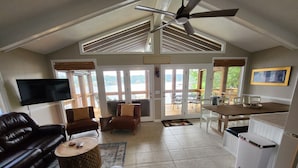 A spacious living area with a large TV, leather sofas, a dining table, and a view of the outdoors. - Lake Front w/ Sunset Views, Screened-in Porch / 1x Boat Slip / 2x Kayaks (Jasper)