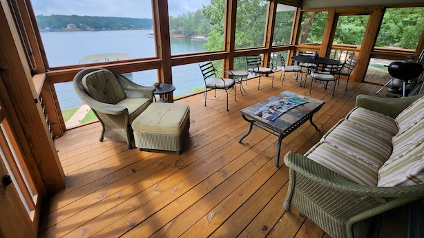 A wooden deck with wicker furniture, a table with magazines, and a view of a lake. - Lake Front w/ Sunset Views, Screened-in Porch / 1x Boat Slip / 2x Kayaks (Jasper)