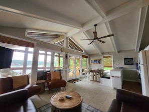 A spacious living area with a large window overlooking a lake, a ceiling fan, and a dining area with a view of the lake. - Lake Front w/ Sunset Views, Screened-in Porch / 1x Boat Slip / 2x Kayaks (Jasper)