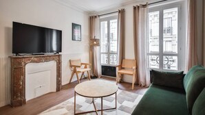 A living room with a fireplace, a television, two chairs, a sofa, and large windows with curtains. - 3.Appart 6Pers#2 Chambres#Commerce#FullEquipped (Paris)