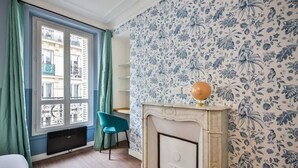 A room with a fireplace, a blue chair, and a window with green curtains. - 3.Appart 6Pers#2 Chambres#Commerce#FullEquipped (Paris)