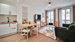 A modern living room with a green sofa, a dining area with a round table and chairs, a flat-screen TV, and a fireplace. - 3.Appart 6Pers#2 Chambres#Commerce#FullEquipped (Paris)