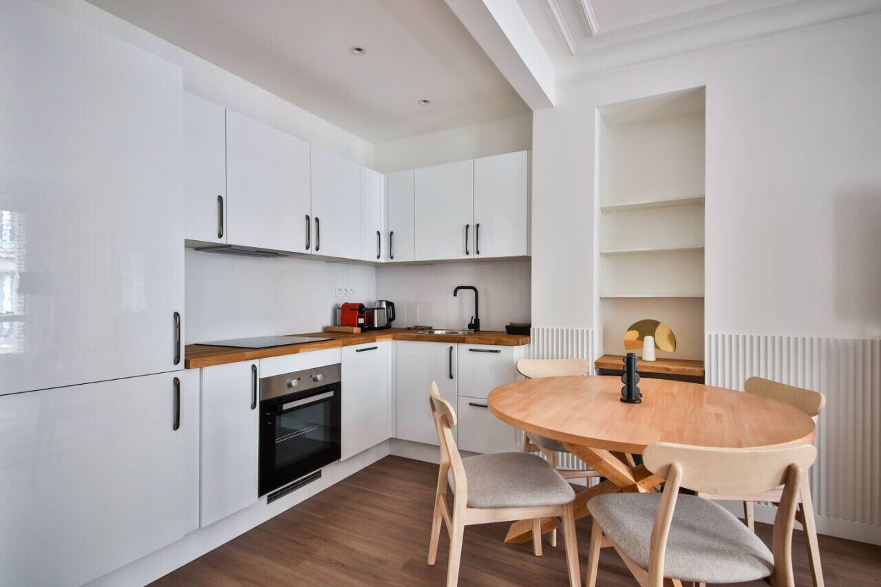 A modern kitchen with white cabinets, a wooden countertop, and a round dining table with chairs.