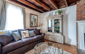 A living room with a brown leather sofa, a glass coffee table, a white cabinet with glass doors, and a brick fireplace.