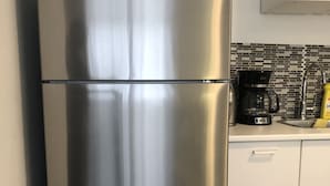 Un refrigerador de acero inoxidable en una cocina con armarios blancos y un salpicadero de azulejos.