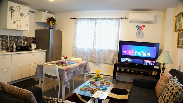 Un espacio habitable compacto con kitchenette, zona de comedor, sofá y televisor que muestra YouTube.