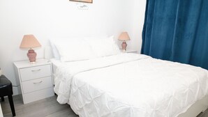 Una cama bien hecha con ropa de cama blanca, dos mesitas de noche con lámparas y una cortina azul.
