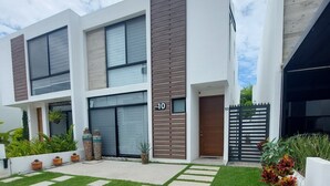 Un edificio moderno de dos pisos con techo plano, ventanas amplias y un patio empedrado con un diseño geométrico de césped y piedra.
