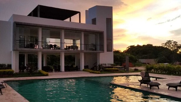 Un moderno edificio de dos pisos con área de piscina, que incluye sillones de descanso y una zona de estar cubierta.