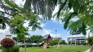 Un parque infantil con tobogán y pared de escalada, rodeado de césped cuidado y árboles.