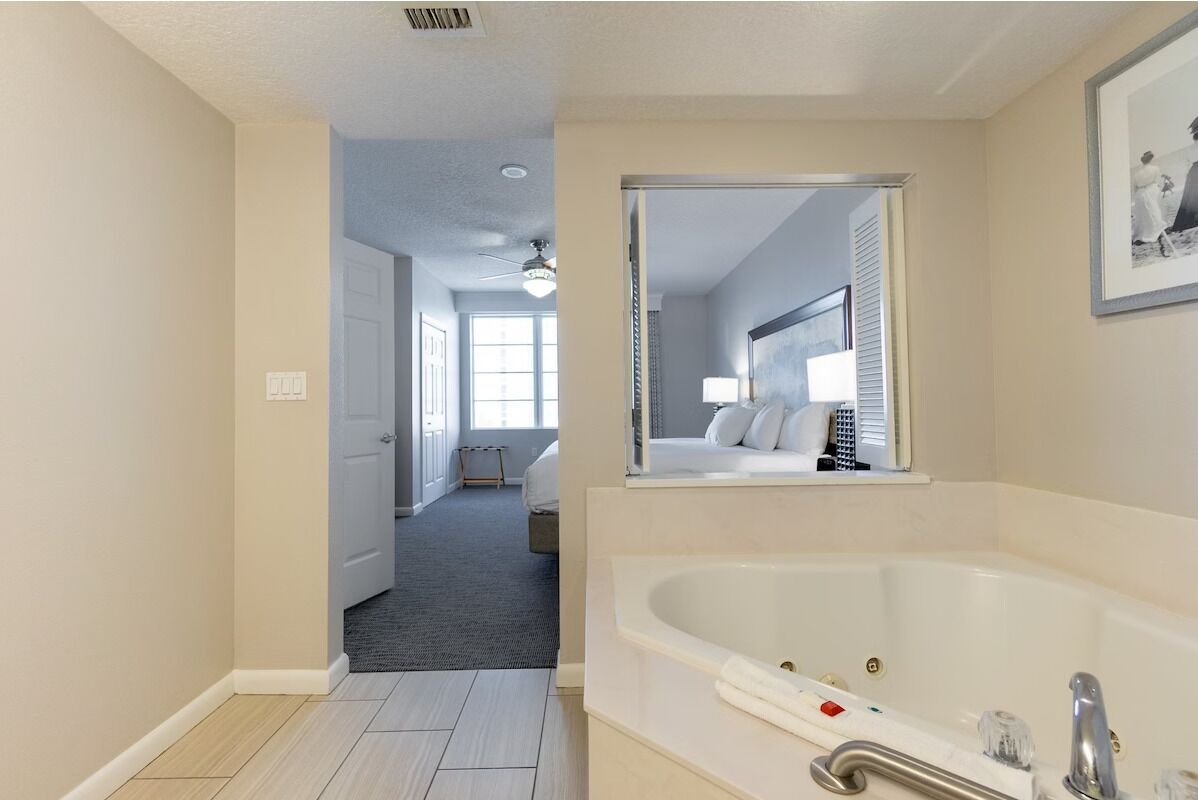 Un bagno moderno con una vasca da bagno ampia, uno specchio e un corridoio che conduce a una camera da letto.