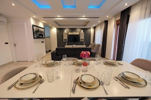 Un comedor con una mesa dispuesta para cuatro personas, un sofá al fondo y un diseño de techo moderno.