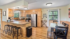 A modern kitchen with wooden cabinets, stainless steel appliances, a central island with stools, and a dining area with a table and chairs. - Lake House Landing w/ view of sailboat cove, quiet street (Garfield)
