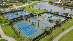 Un complex de pistes de tennis amb diverses pistes, envoltat de verdura i un llac.