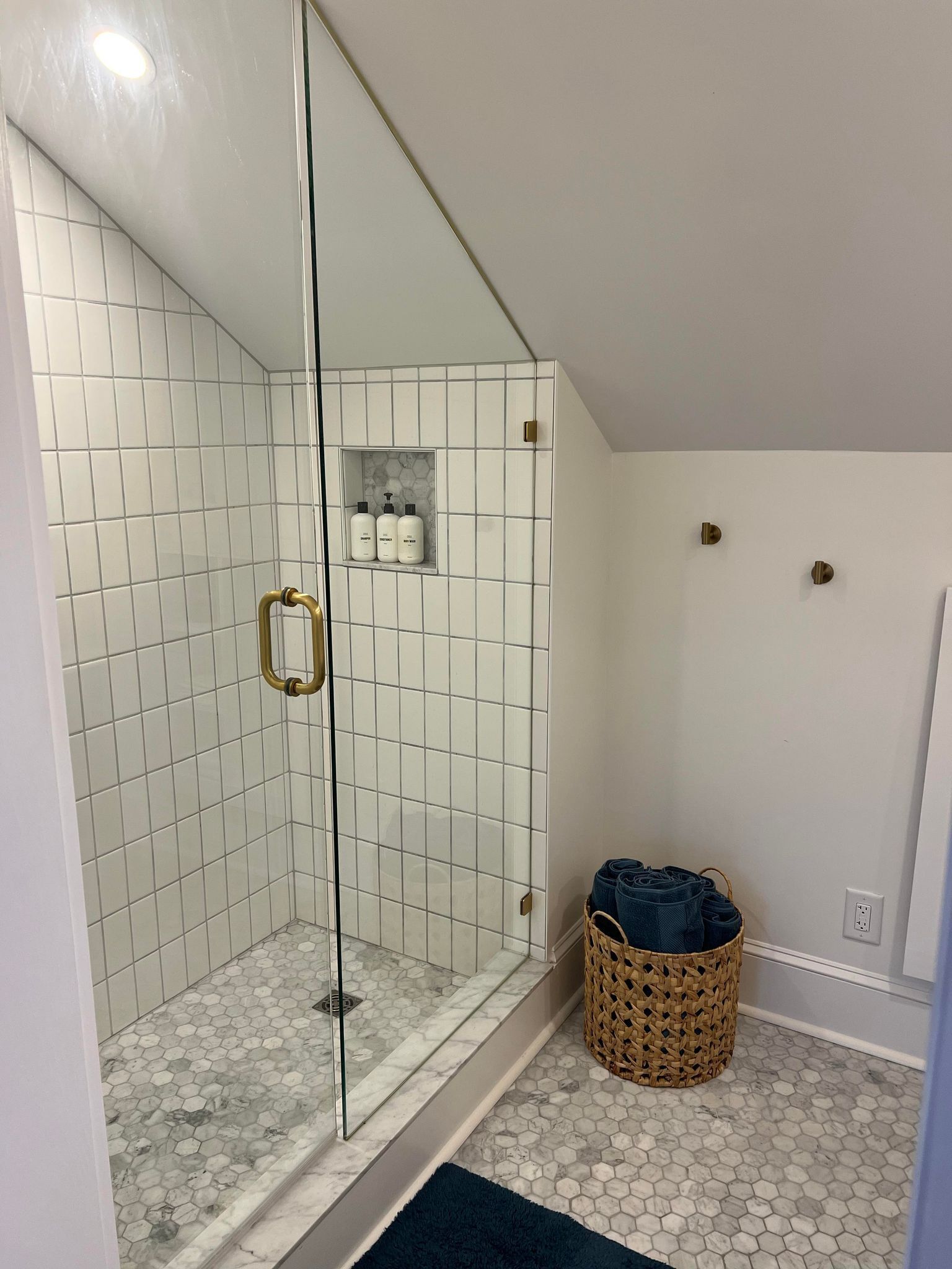 Eine Dusche mit weißen Fliesen, einer Glastür und einer kleinen Ablage für Toilettenartikel.