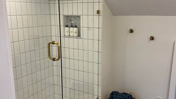 Eine Dusche mit weißen Fliesen, einer Glastür und einer kleinen Ablage für Toilettenartikel.
