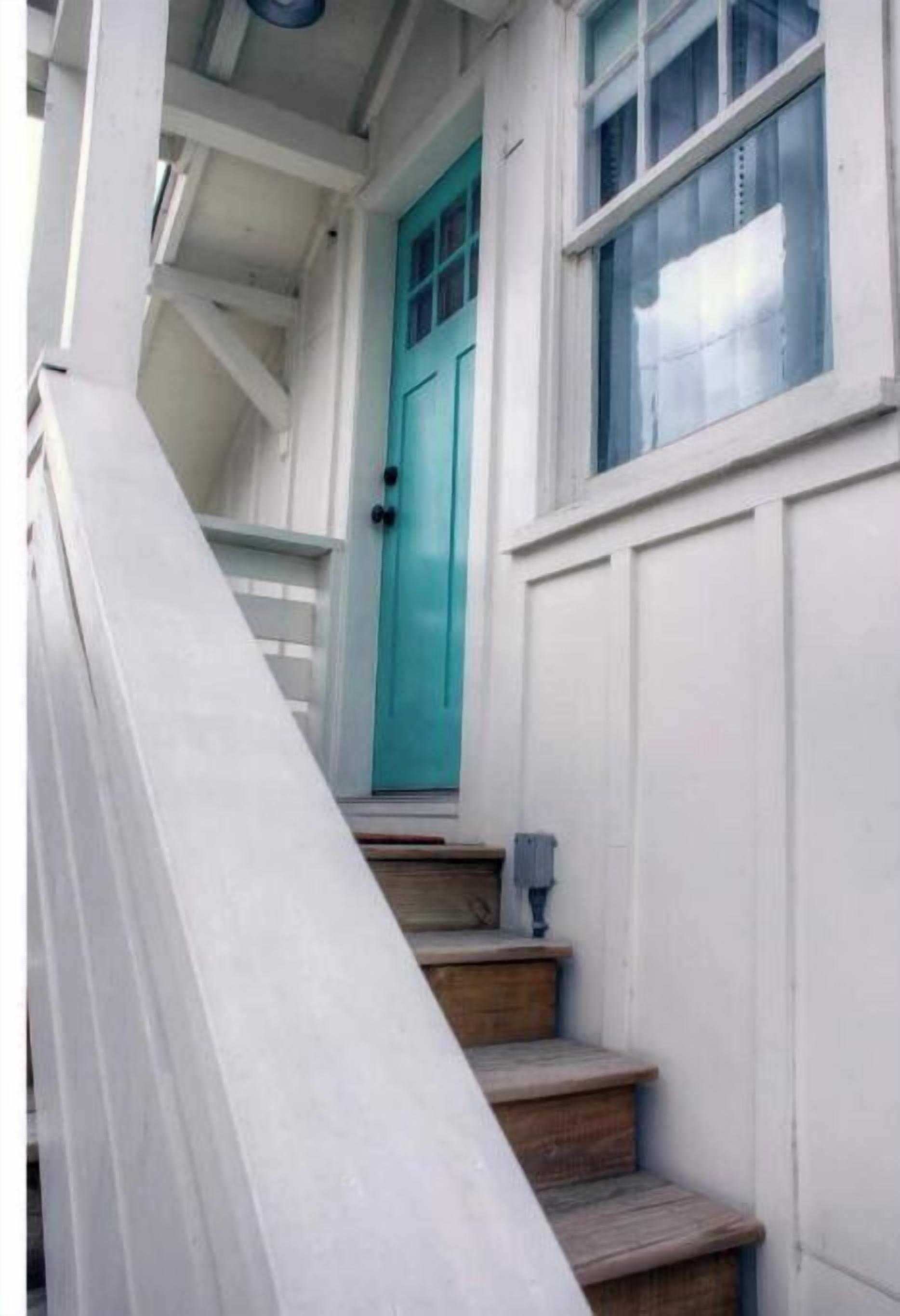 A staircase leading to a turquoise door with a window above it.