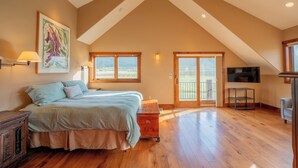 Une chambre spacieuse avec un grand lit, un plancher en bois, un tableau au mur et un téléviseur.
