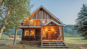 Un chalet rustique en bois, doté d’un balcon, d’un porche et surplombant un paysage montagneux.