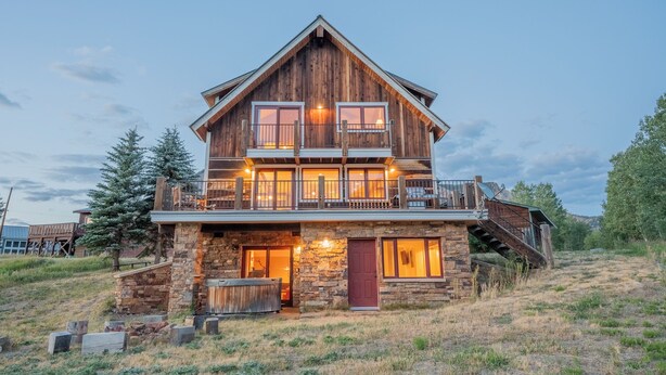 Une cabane en rondins à deux étages, avec des fondations en pierre, un balcon en bois et une cheminée en pierre.