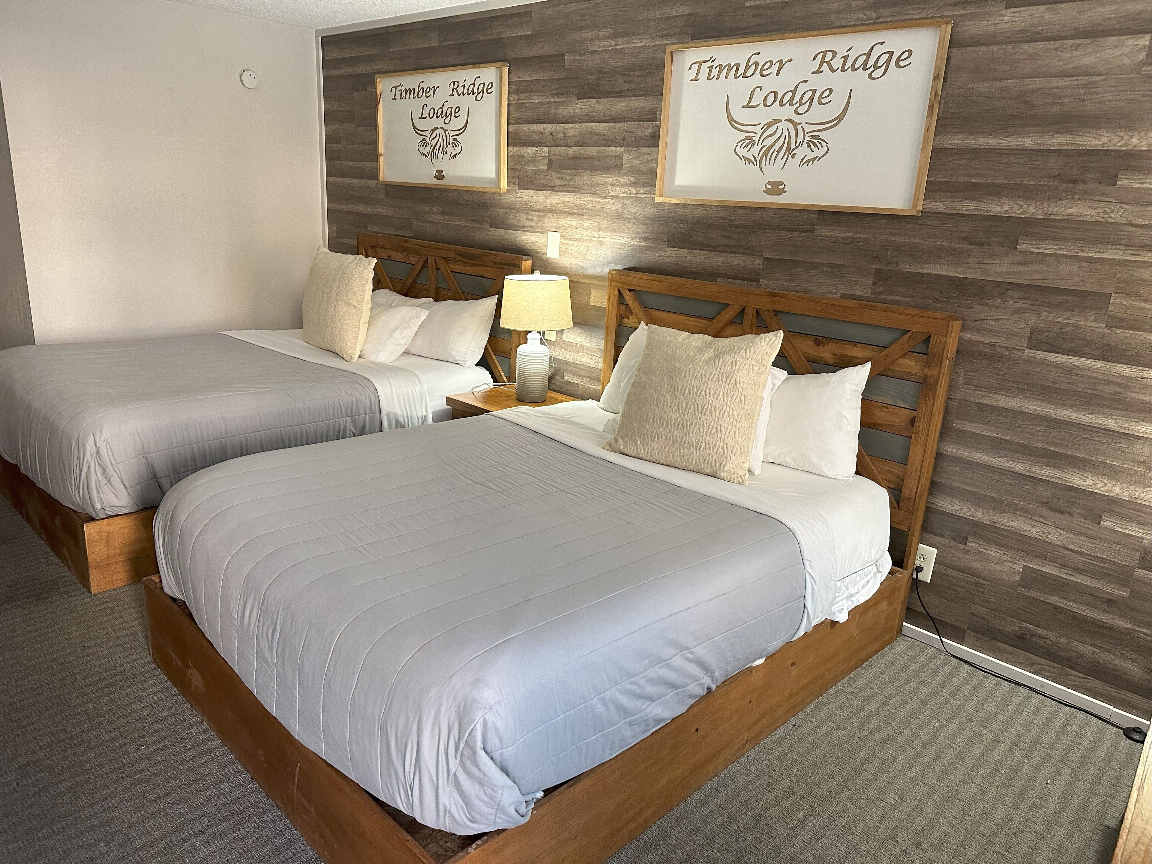 Un letto matrimoniale con testiera in legno, due comodini con lampade e un cartello appeso al muro con la scritta "Timber Ridge Lodge".