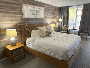 A neatly arranged bedroom with a bed, two bedside tables, a framed sign above the bed, and a view of the outdoors through a window. - Timber Ridge Lodge - Walking Distance from Downtown Gatlinburg (Gatlinburg)