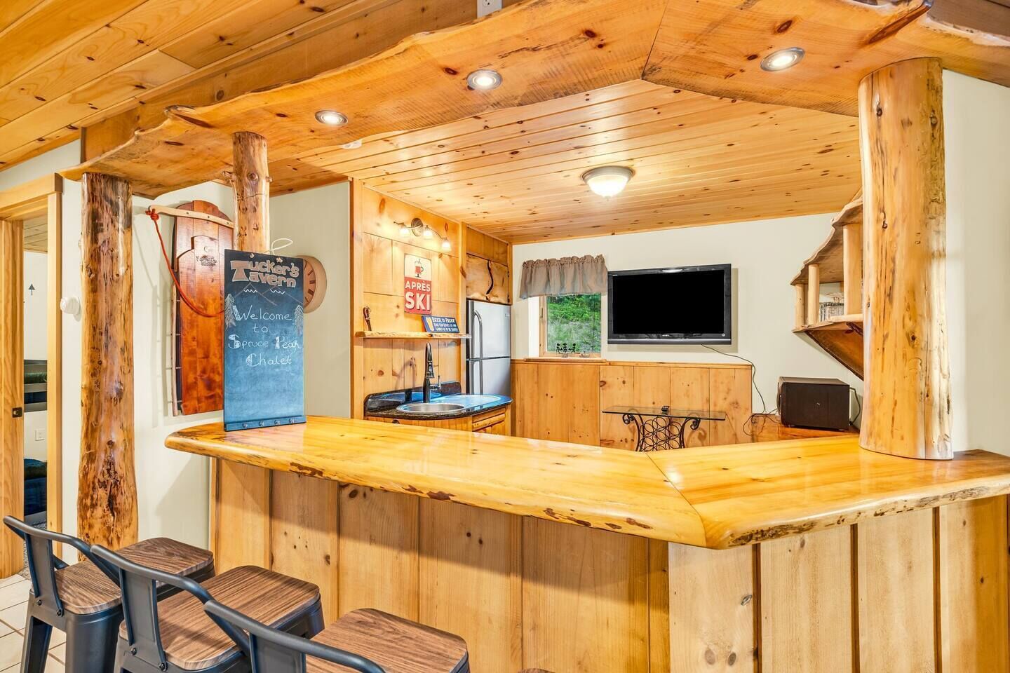 A wooden bar area with a chalkboard sign, a television, and a window with a view of greenery.