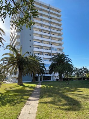 A multi-story building with balconies, a paved pathway, and palm trees.