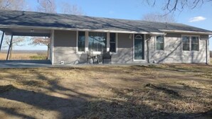 A single-story house with a covered porch, a small patio, and a view of a field. - The Jadwin House LLC, Located in Jadwin, Missouri, sleeps 14 guests. (Jadwin)