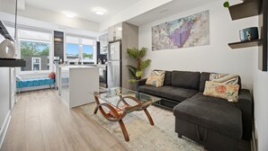 A modern living room with a glass coffee table, a dark sofa, and a large abstract painting on the wall. - Exquisite, bright &modern 2 bedroom condo/Free Parking (Niagara Falls)