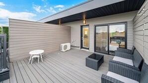 A modern outdoor deck with a white table and chairs, a black sofa, and a glass door leading to a covered area. - Exquisite, bright &modern 2 bedroom condo/Free Parking (Niagara Falls)