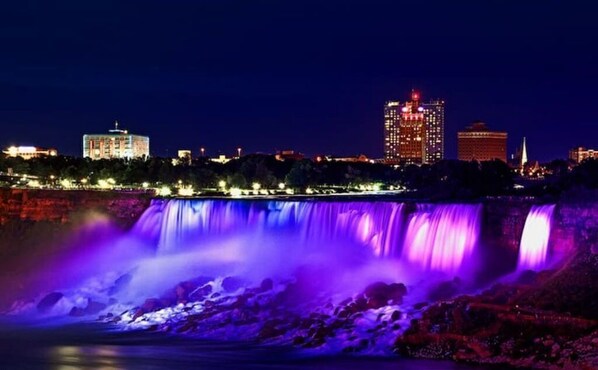 A nighttime view of a cityscape with a waterfall illuminated by purple lights.