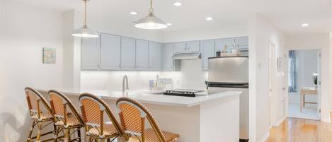 A modern kitchen with white cabinets, a central island with bar stools, stainless steel appliances, and pendant lighting.