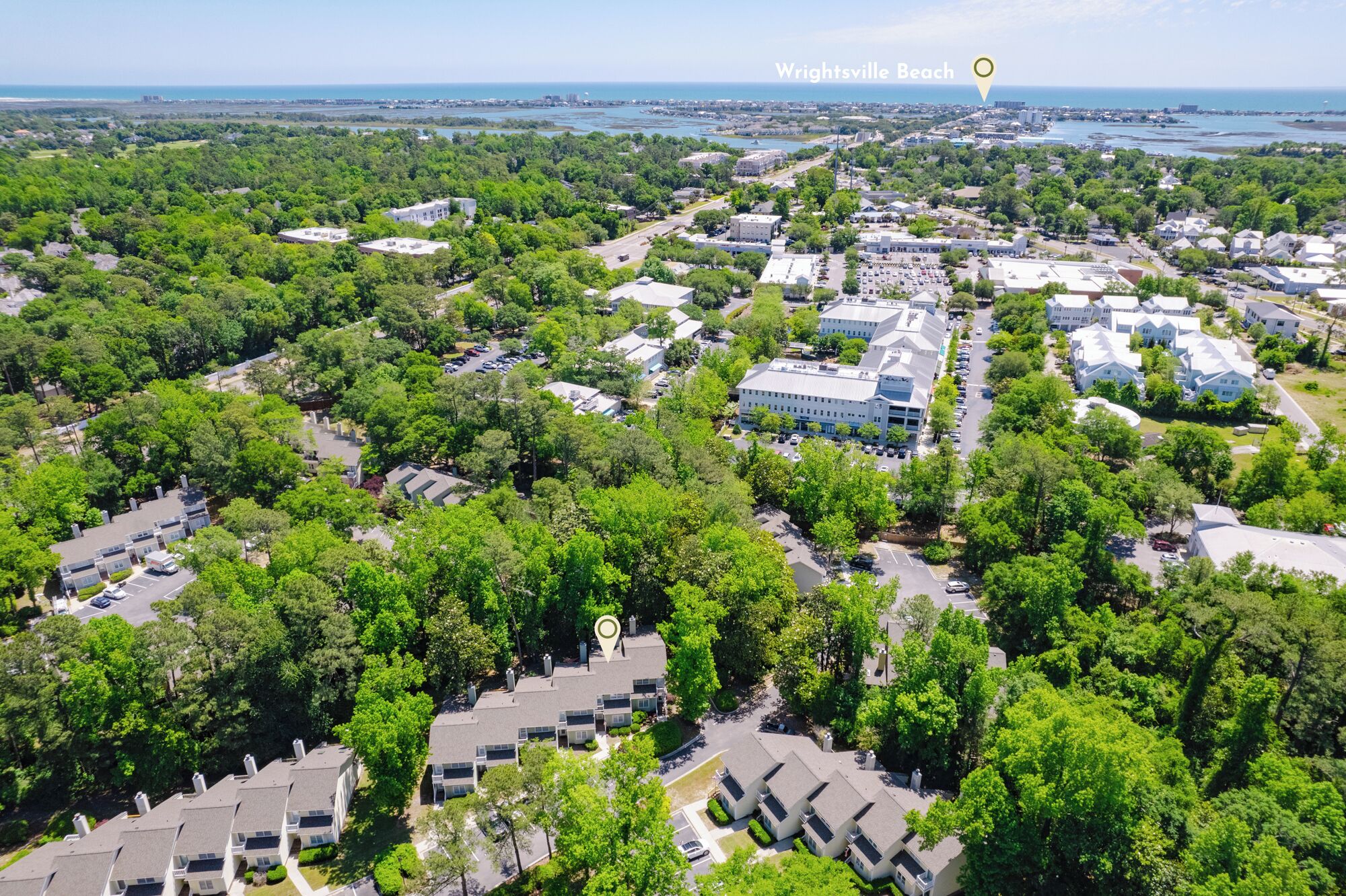 An aerial view of a residential area with a mix of single and multi-story buildings, surrounded by dense greenery.