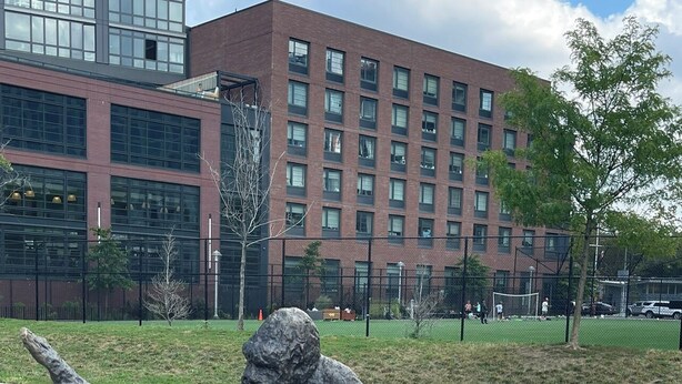 En skulptur av en elefant placerad på en vit piedestal, försedd med inskriptioner på flera språk, och som står på ett torg med en byggnad och träd i bakgrunden.