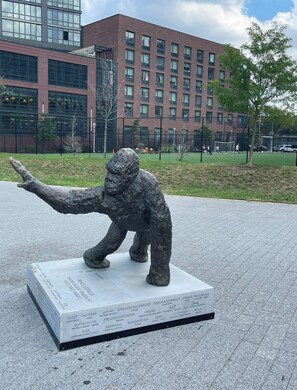 A sculpture of an elephant on a white pedestal with multilingual inscriptions, set in a plaza with a building and trees in the background. - The Best Views In Brooklyn (Brooklyn)