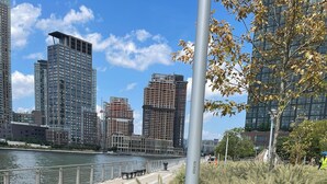 En strandpromenad längs floden med stadens silhuett som bakgrund, där moderna höghus syns.