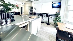 Een moderne keuken met een roestvrijstalen kookeiland, barstoelen en een aan de muur bevestigde televisie.